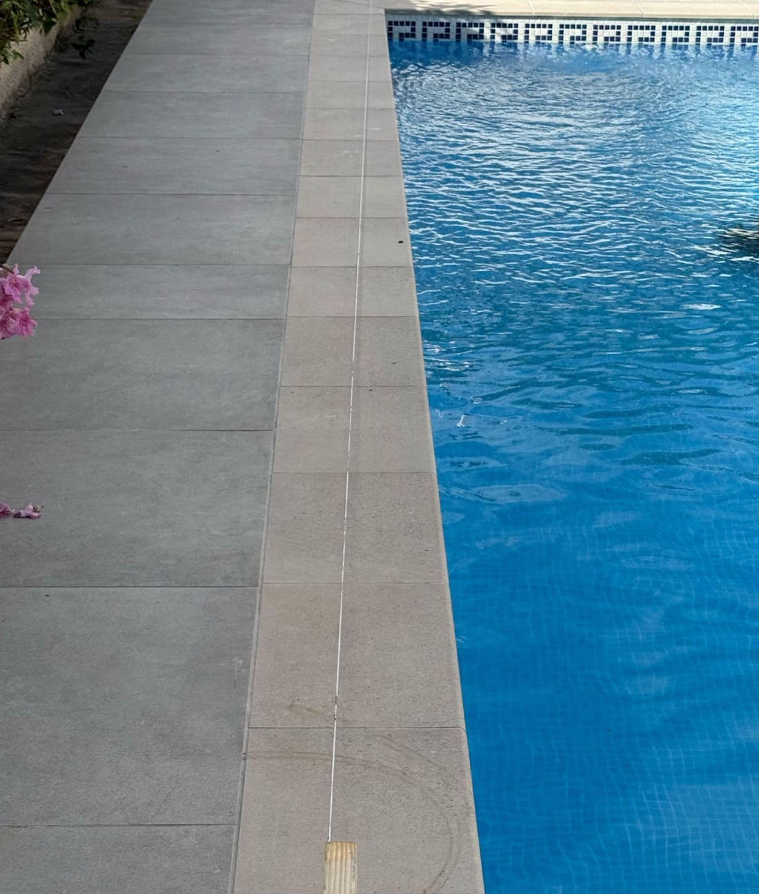 At the far end, the proposed line (white string) has crept right up to the pool edge — visibly off the tile grid.